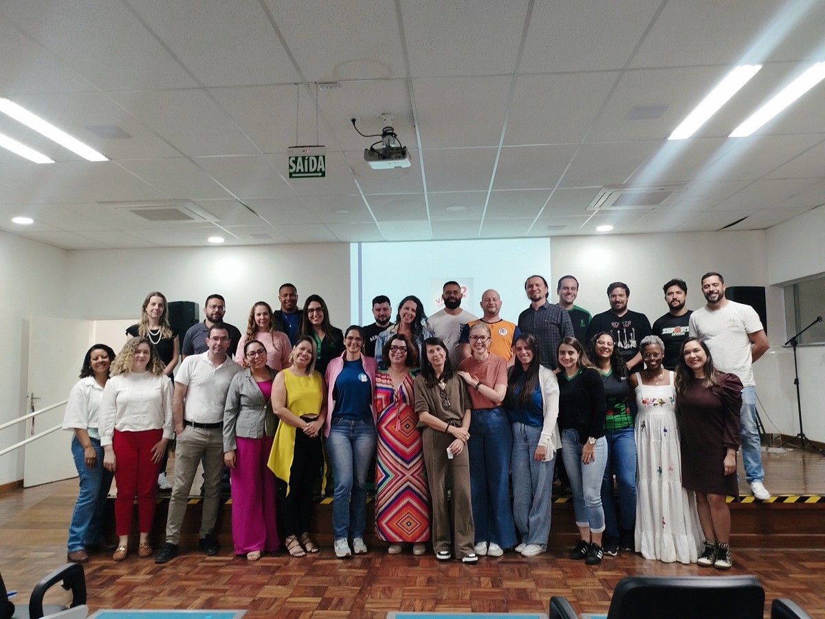 Foto em grupo com cerca de 30 servidores do campus e a palestrante, todos em pé e sorrindo, posicionados no palco do auditório após o evento.